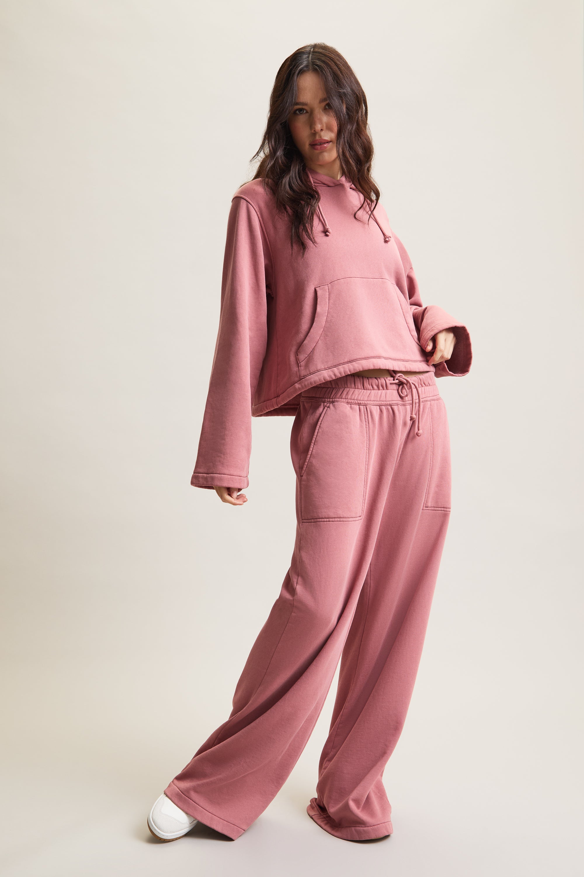 Women's HRMN8 dusty pink cropped hoodie with wide sleeves, central pocket, and adjustable drawstring hood. Made from soft, heavyweight fabric with a smooth lining for comfort. Features subtle silicone branding on the front. Perfect for athleisure, loungewear, and layering. Styled with matching joggers for a modern, relaxed fit.