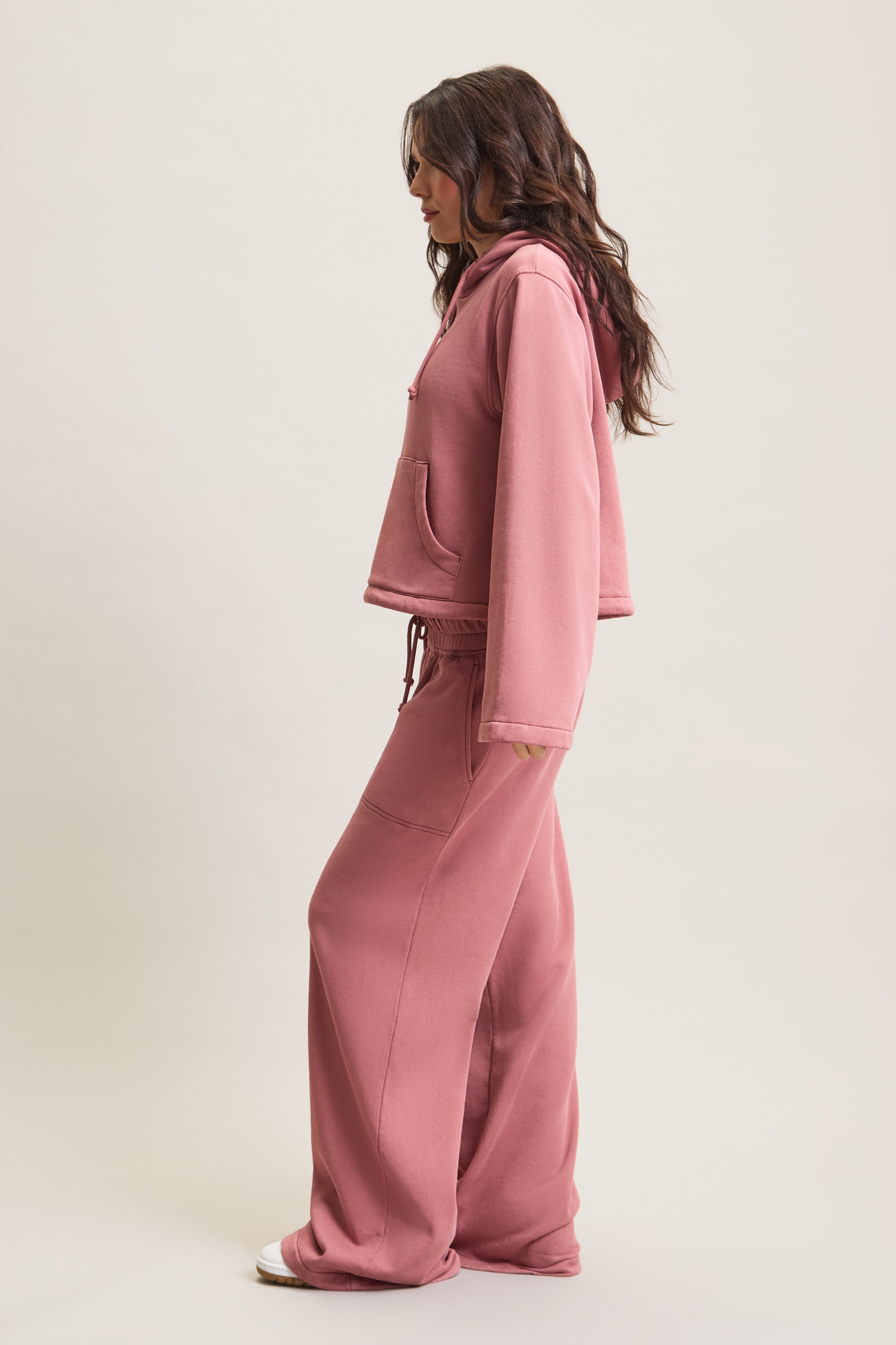 Women's HRMN8 dusty pink cropped hoodie with wide sleeves, central pocket, and adjustable drawstring hood. Made from soft, heavyweight fabric with a smooth lining for comfort. Features subtle silicone branding on the front. Perfect for athleisure, loungewear, and layering. Styled with matching joggers for a modern, relaxed fit.