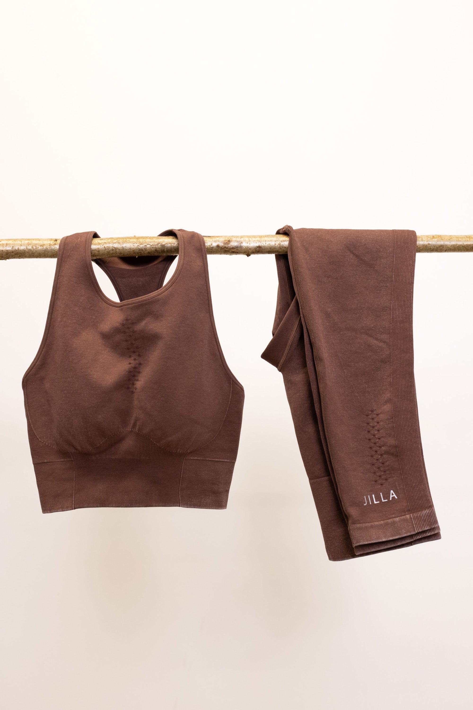 Meet our chocolate brown Aquarius Recycled Sports Bra - uniquely textured and stylish, perfect for yoga, barre, and more. Crafted from soft recycled seamless fabric, it offers light to medium support with a high neckline and statement back shape. Pair with our matching leggings for a seamless studio-to-street look. Enjoy versatile support and comfort, customizable with removable pads by sustainable activewear brand Jilla Active