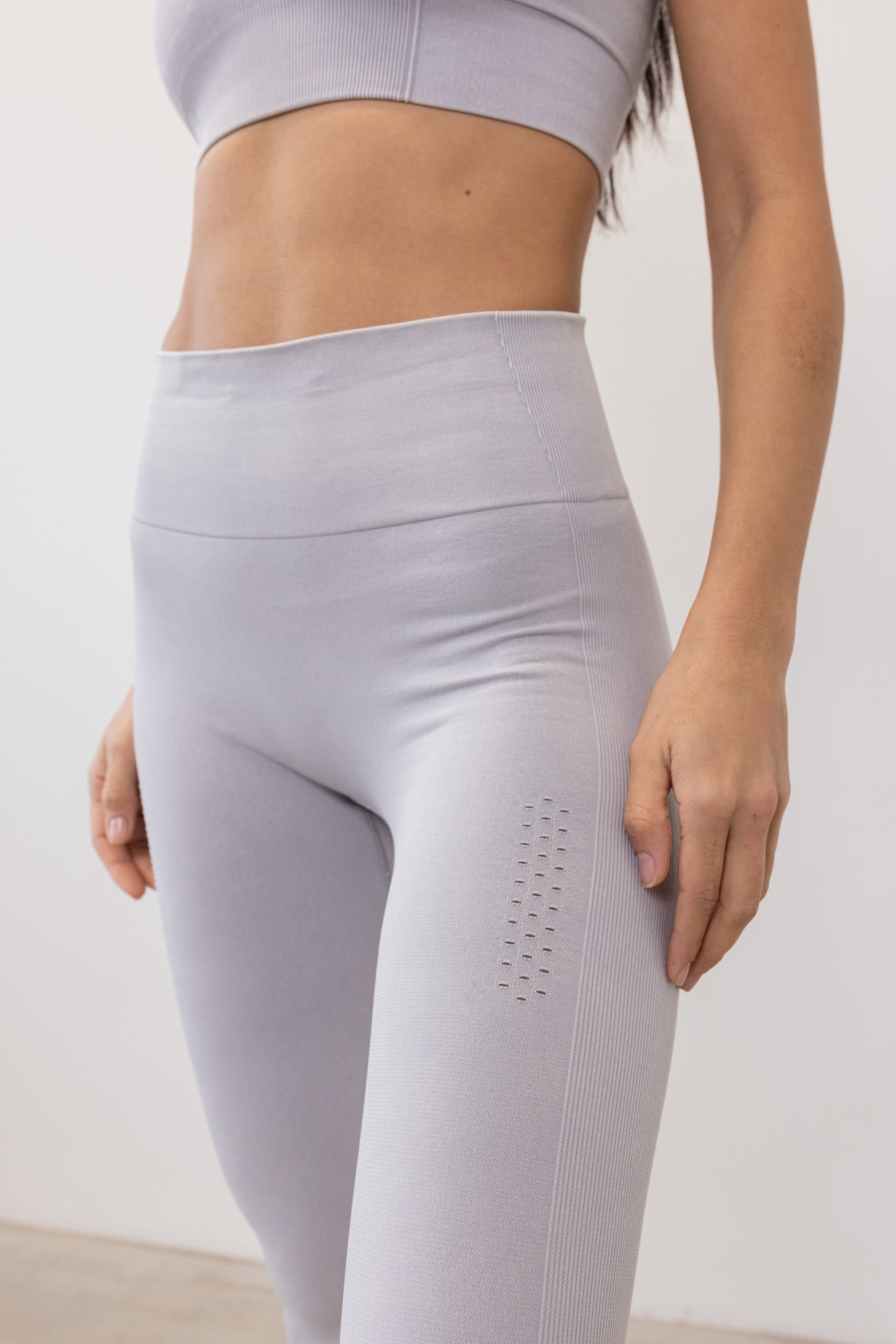 Our light grey Aquarius Recycled Leggings - crafted for seamless performance in your yoga flows, barre workouts, and reformer classes. Made from four-way stretch fabric, they move effortlessly with you. Designed with flattering ribbing and an acid wash effect, each pair is unique. The high-rise ribbed waistband with internal elastic ensures they stay in place during your entire class, while the double-layered gusset provides all-day comfort and flexibility. 