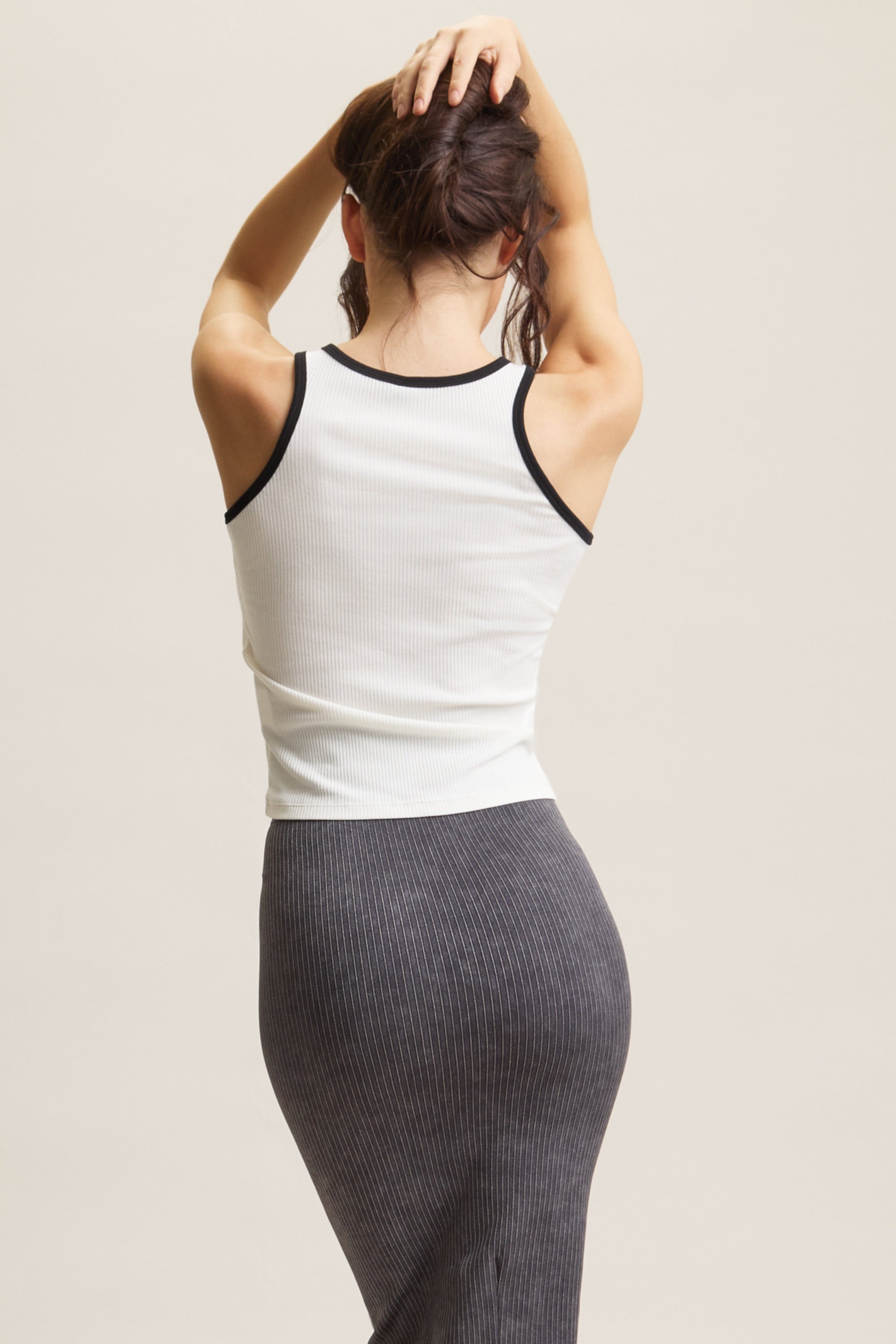 Women's HRMN8 white Spry Tank, made from soft rib fabric, offers a comfortable second-skin feel with just the right amount of stretch. Featuring a flattering cut-in neckline and contrast binding at the neck and armholes, this modern tank top is perfect for athleisure wear. Subtle silicone branding at the hem adds a sleek touch. Ideal for pairing with the Take Over Maxi Skirt for an elevated athleisure look, this versatile top can be worn solo or layered, perfect for athleisure, workouts, Pilates, gym wear, 